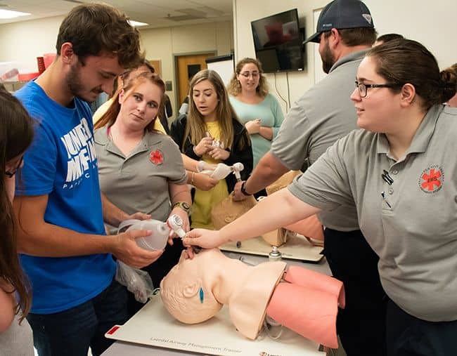 Students practicing CPR techniques on a medical mannequin during a healthcare program class.