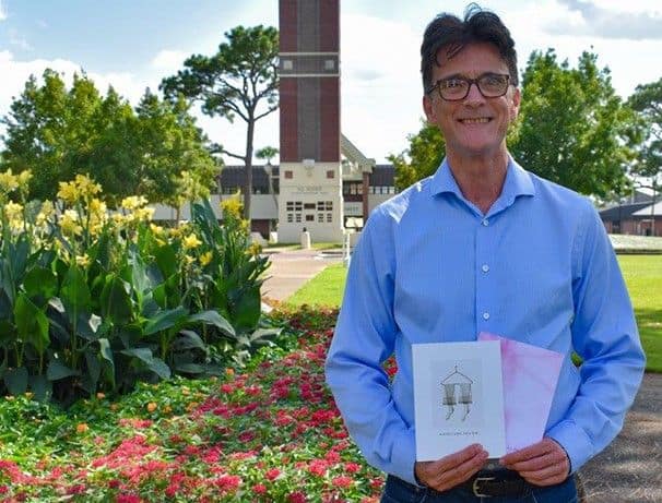 Jamey Jones, PSC instructor and Poet Laureate, standing outdoors with flowers and campus buildings.
