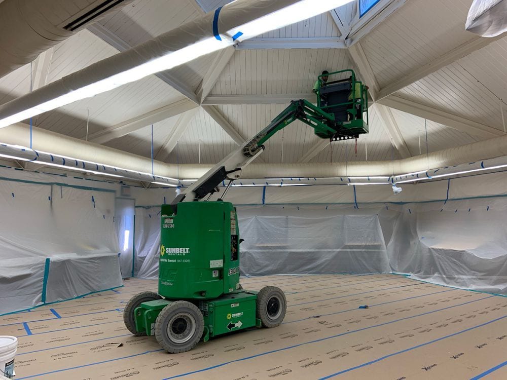 Mobile aerial lift in a large, covered space with protective plastic sheeting on the walls.