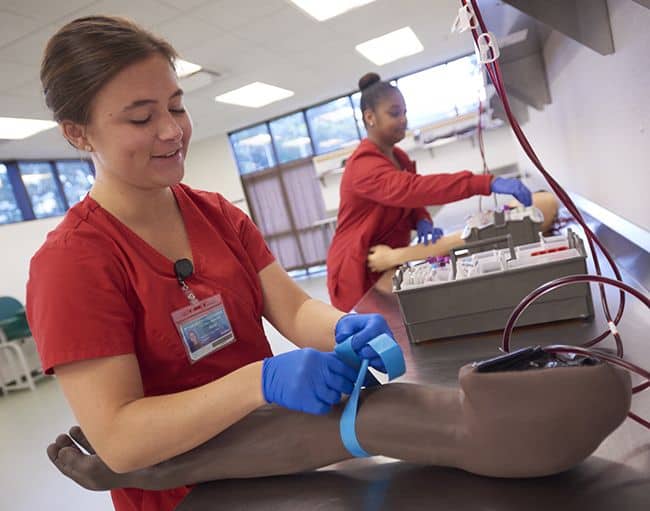 Students in medical scrubs and gloves performing clinical skills training.