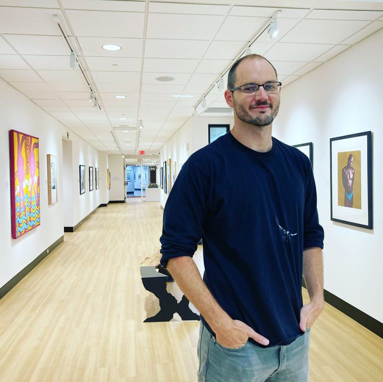 Art gallery director at Pensacola State College showcasing artwork in a modern gallery space.