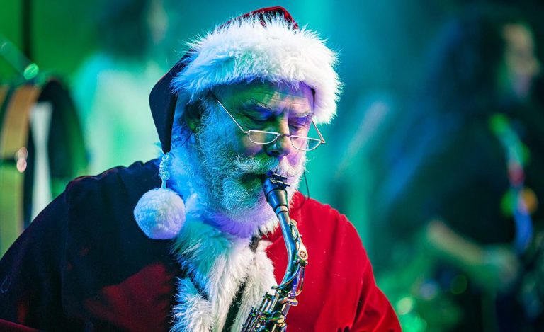 Santa Claus playing saxophone during college holiday celebration.