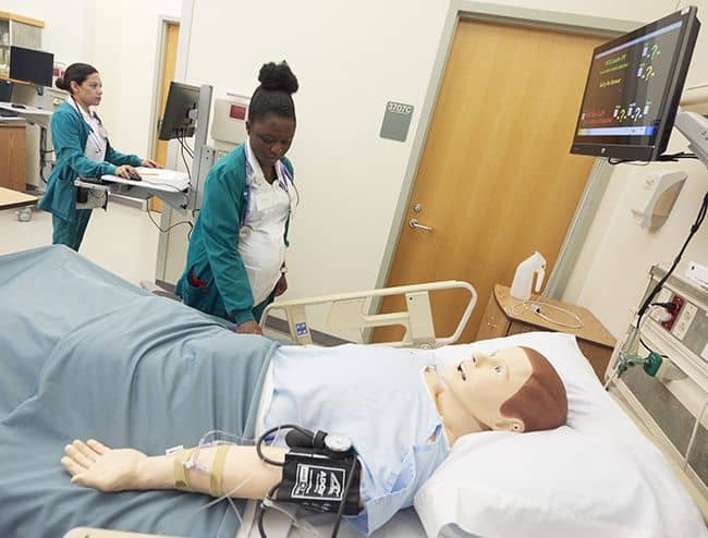 Nursing students at Pensacola State College practicing patient care skills with simulation mannequin.