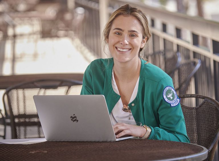 Highly accessible image of a smiling nursing student with laptop outdoors.