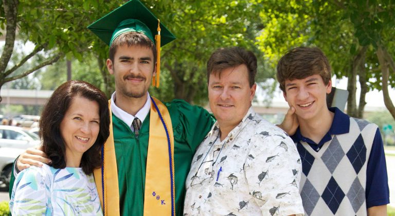 High school graduate Kyle Lowrey with family during graduation ceremony at Pensacola State College.