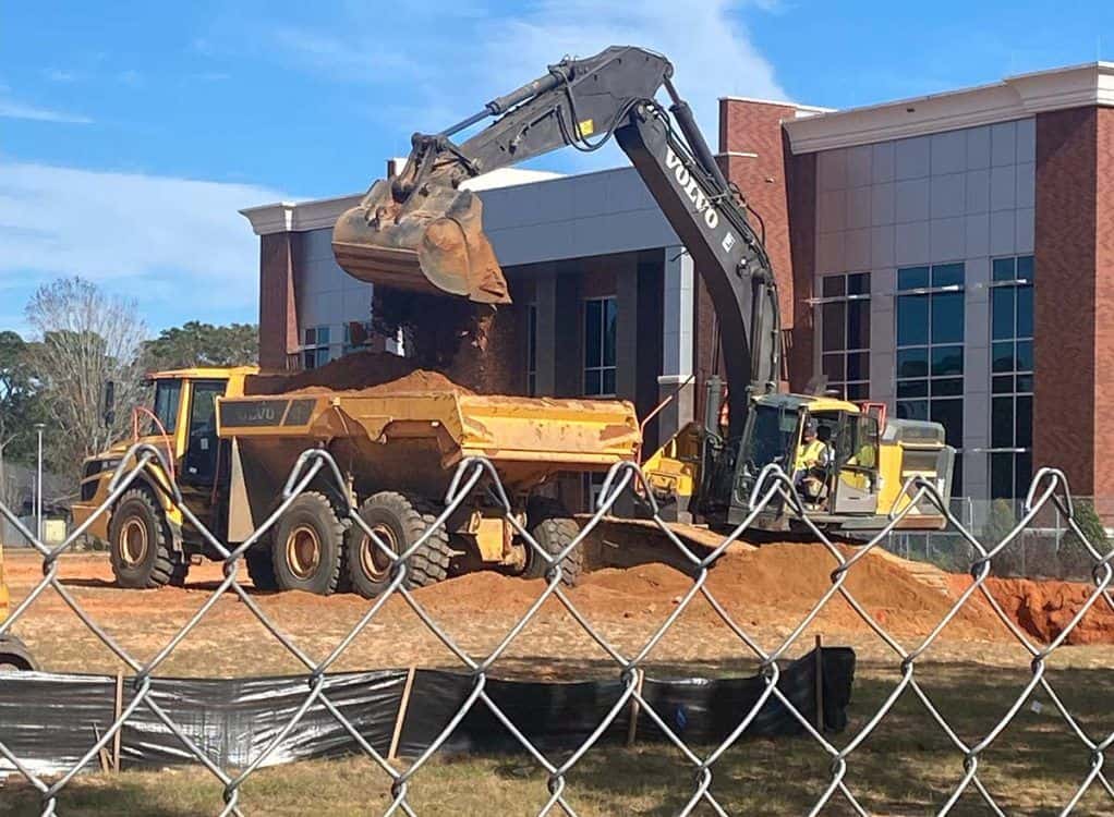 Excavator loading soil during campus expansion for IT and cybersecurity programs.