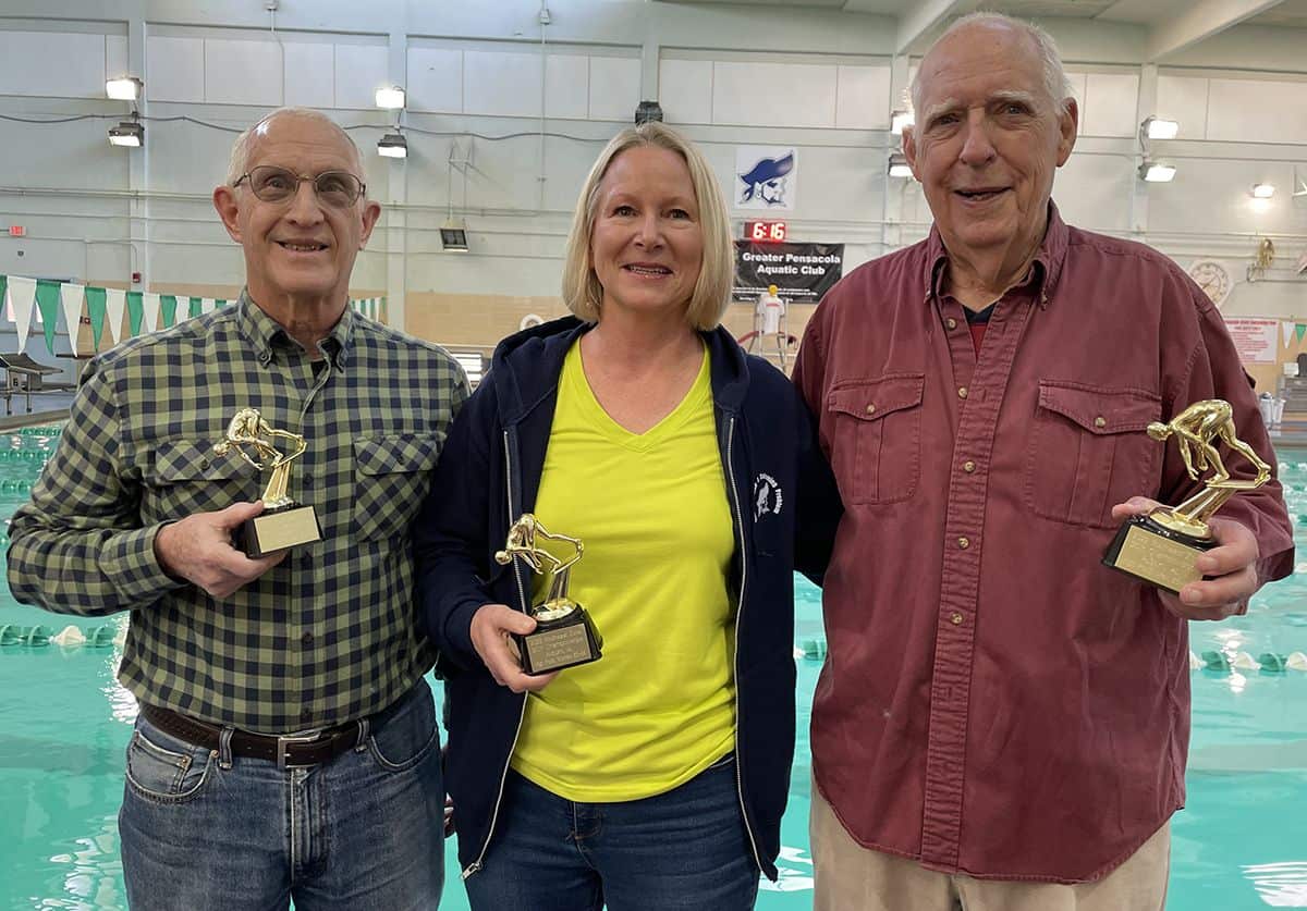 An image of three smiling team members holding trophies after winning at the Auburn Masters SCY Invi.