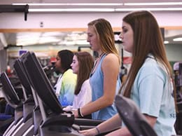 High school students engaging in fitness activities on treadmills at Pensacola State College gym.