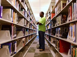 Student browsing books in college library aisle at Pensacola State College.