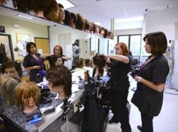 Hair styling students practicing techniques in a college classroom setting.