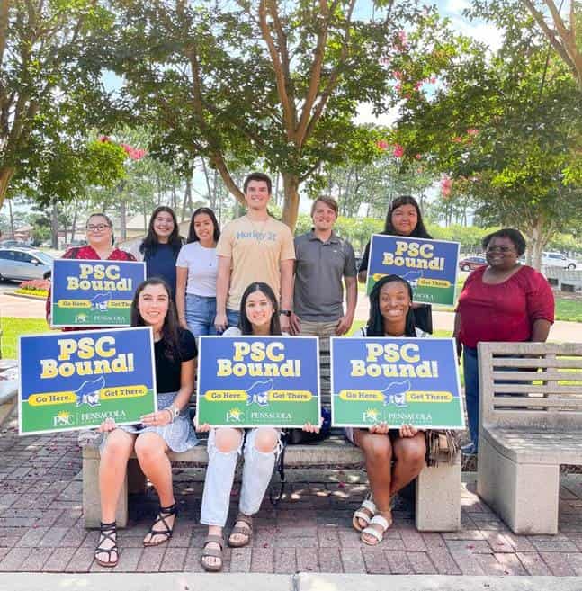College student ambassadors holding signs for Pensacola State College at an outdoor event.