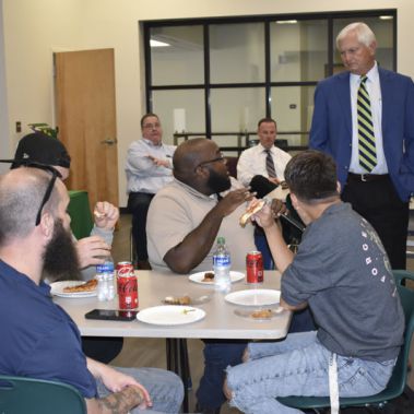 President interacts with diverse students enjoying pizza in a college event.