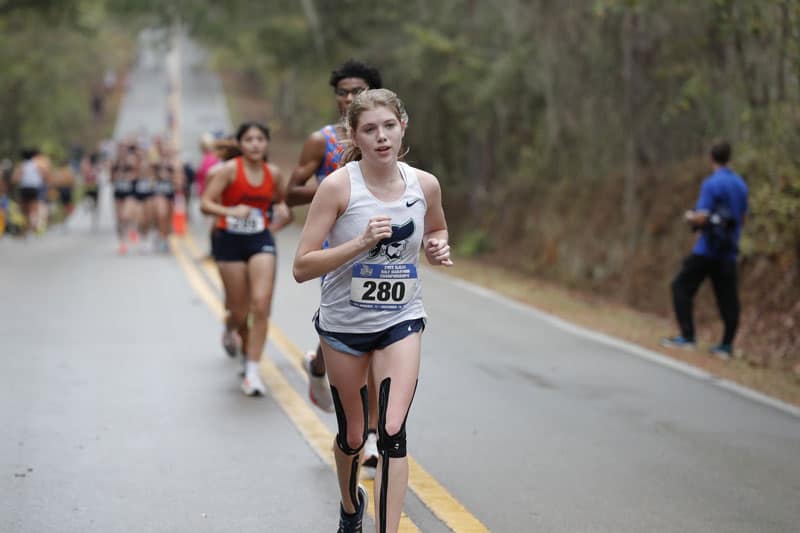 Female college cross country runner with prosthetic leg during race at national event.