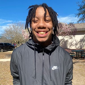 Young male student smiling outdoors at Pensacola State College campus in sunny weather.