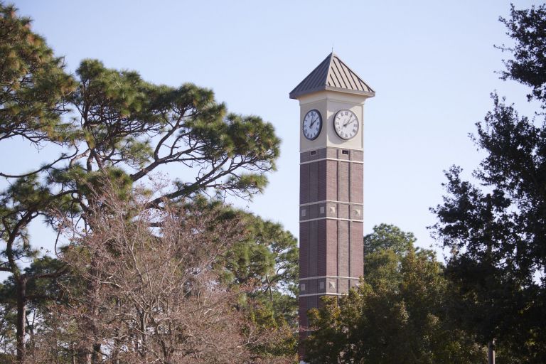 Clock tower on Pensacola State College campus, Florida, surrounded by trees.