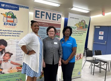 Three women standing at UF/IFAS Extension Escambia County event with banners in background.
