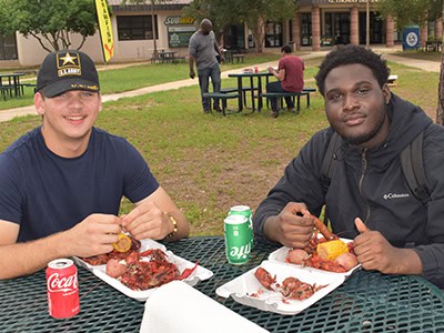 Two students enjoying crawfish and barbecue at a college outdoor event.