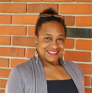 Accessible image of a confident student smiling against a brick wall, representing TRIO Student Supp.