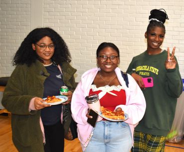 Students smiling with pizza and drinks at college gathering.