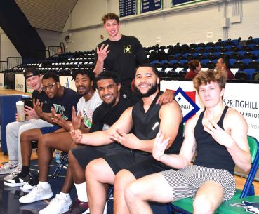 Students sitting on bleachers, smiling, and making hand gestures during a college sports game.