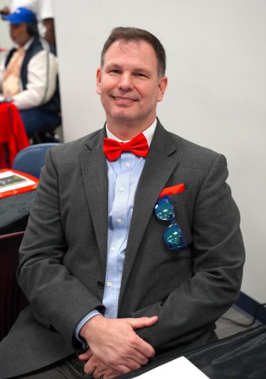 Dressed in a gray suit with a red bow tie, smiling at the event.