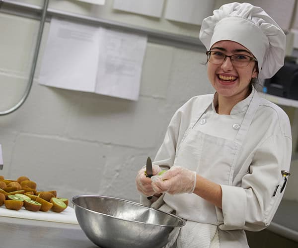Culinary student in chef uniform smiling while preparing food for CTE Month event at Pensacola State.