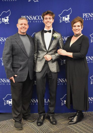Smiling young man in tuxedo with parents at graduation event.