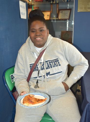 Student with a hoodie and basketball sweatshirt holding a slice of pizza.