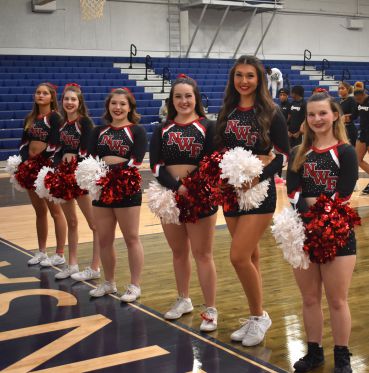Cheerleaders in black and red uniforms holding pom-poms at Pensacola State College gymnasium.