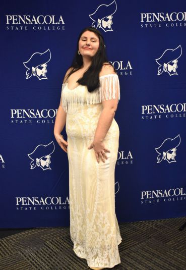 A woman in a cream-colored dress standing confidently at Pensacola State College graduation event.