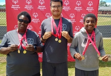 Diverse team member proudly displays medals at Special Olympics event on campus.