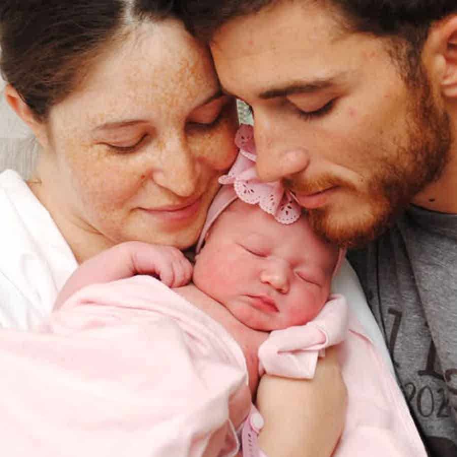 Close-up of proud parents holding newborn baby during graduation celebration at Pensacola State Coll.