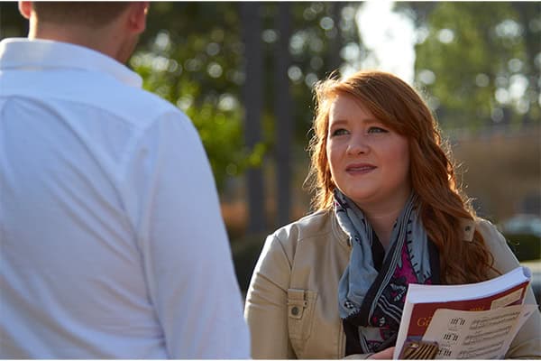 Woman discussing scholarship options with veteran family member outdoors.