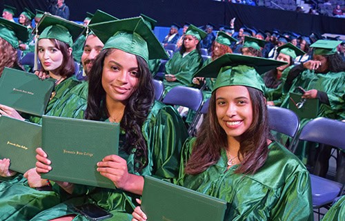 Graduates in green caps and gowns celebrating December graduation at Pensacola State College.