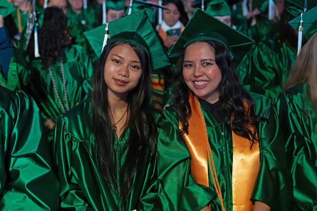 Students in green caps and gowns celebrating graduation at Pensacola State College.